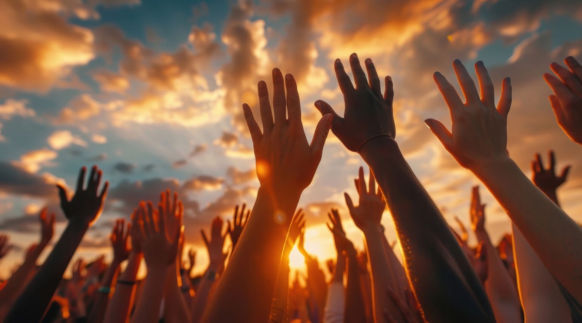 Hands raised in prayer and praise against a golden sunset sky